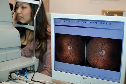 A patient at the retinal camera with fundus photographs on screen